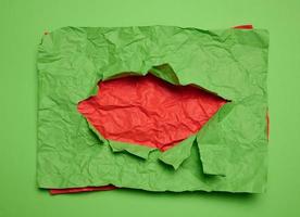 Texture of crumpled green paper with torn hole and red background photo