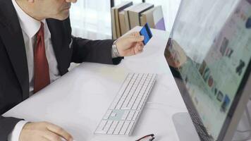 Office worker holding credit card using instant mobile payment in office. Man is shopping from Online internet stores from his computer. video