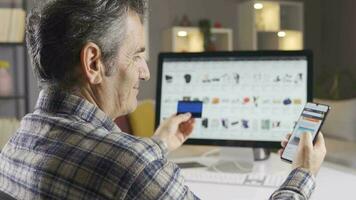 A man browsing and researching online shopping sites to buy new products. The man is shopping online from his home computer and phone. video