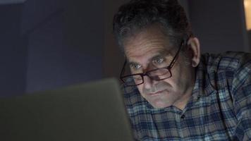 Focused and serious man looking at laptop at home. Mature man looking at laptop at night at home doing serious work and focusing. video