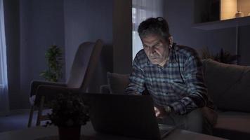 Man working from home looking at laptop and seeing something bothering him and getting upset. Man working remotely from home at night doing his work on laptop over internet feeling upset and stressed. video