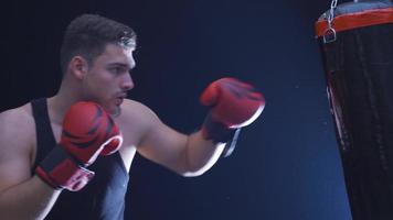 stark Athlet Schläge Stanzen Tasche im staubig Fitnessstudio. filmisch Boxen Szene. jung Boxer Prügel das Stanzen Tasche, Ausbildung Tag beim das Boxen Fitnessstudio, stark Körper. video