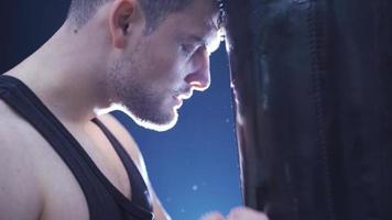 Tired male boxer training nonstop, not giving up. Close-up Male boxer punching a punching bag. Focused and serious male boxer. video