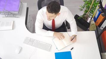 Businessman works in the office. Businessman working with computer in his office making notes in notebook. video