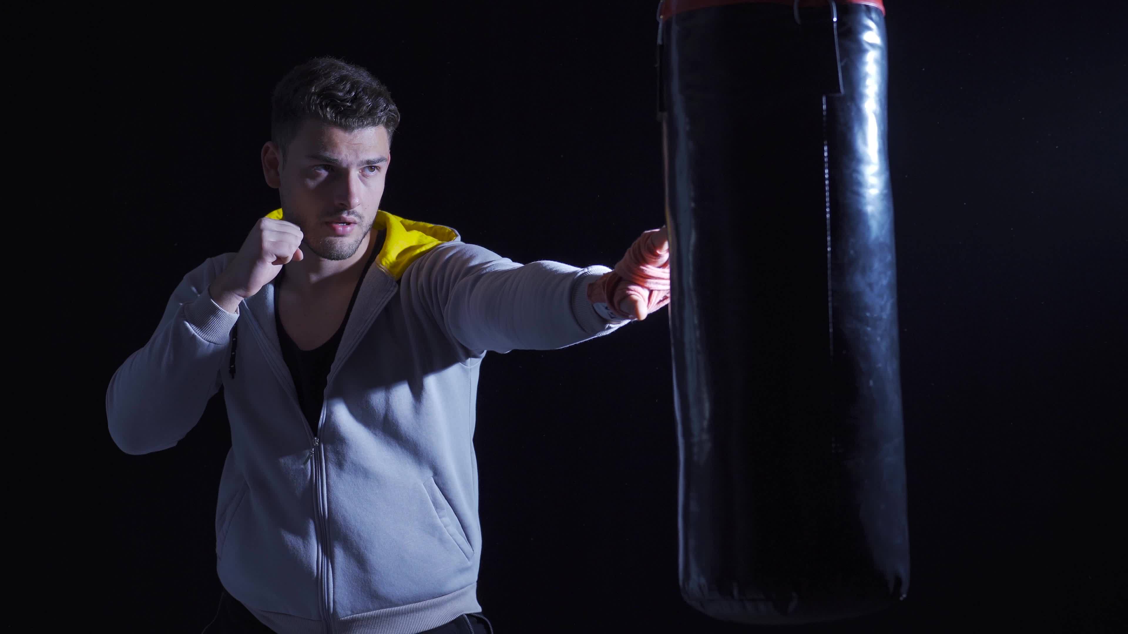 Boxer young man punching punching bag in dark gym. Young Boxer Beating