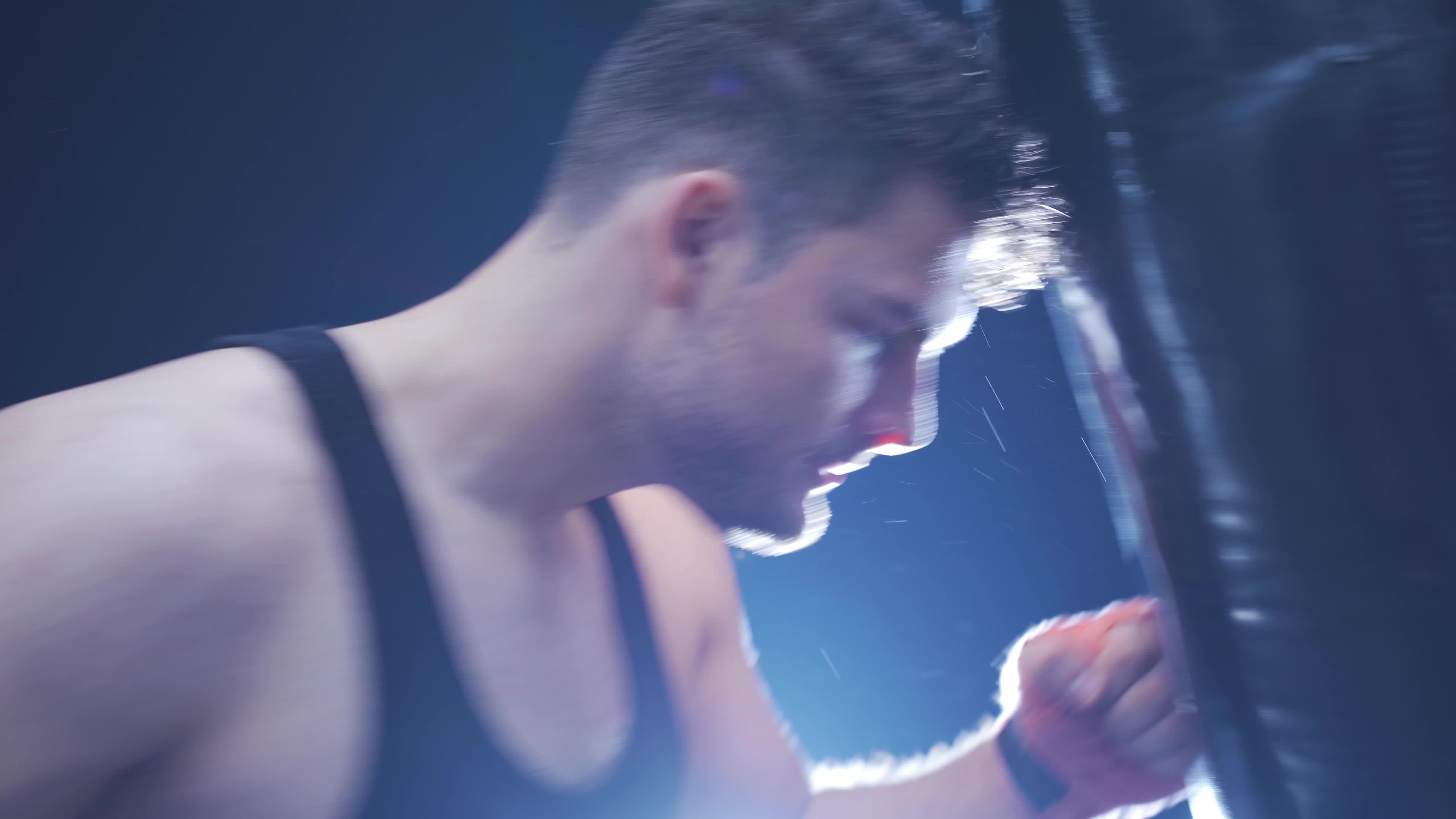 Tired male athlete training boxing with punching bag in dark gym