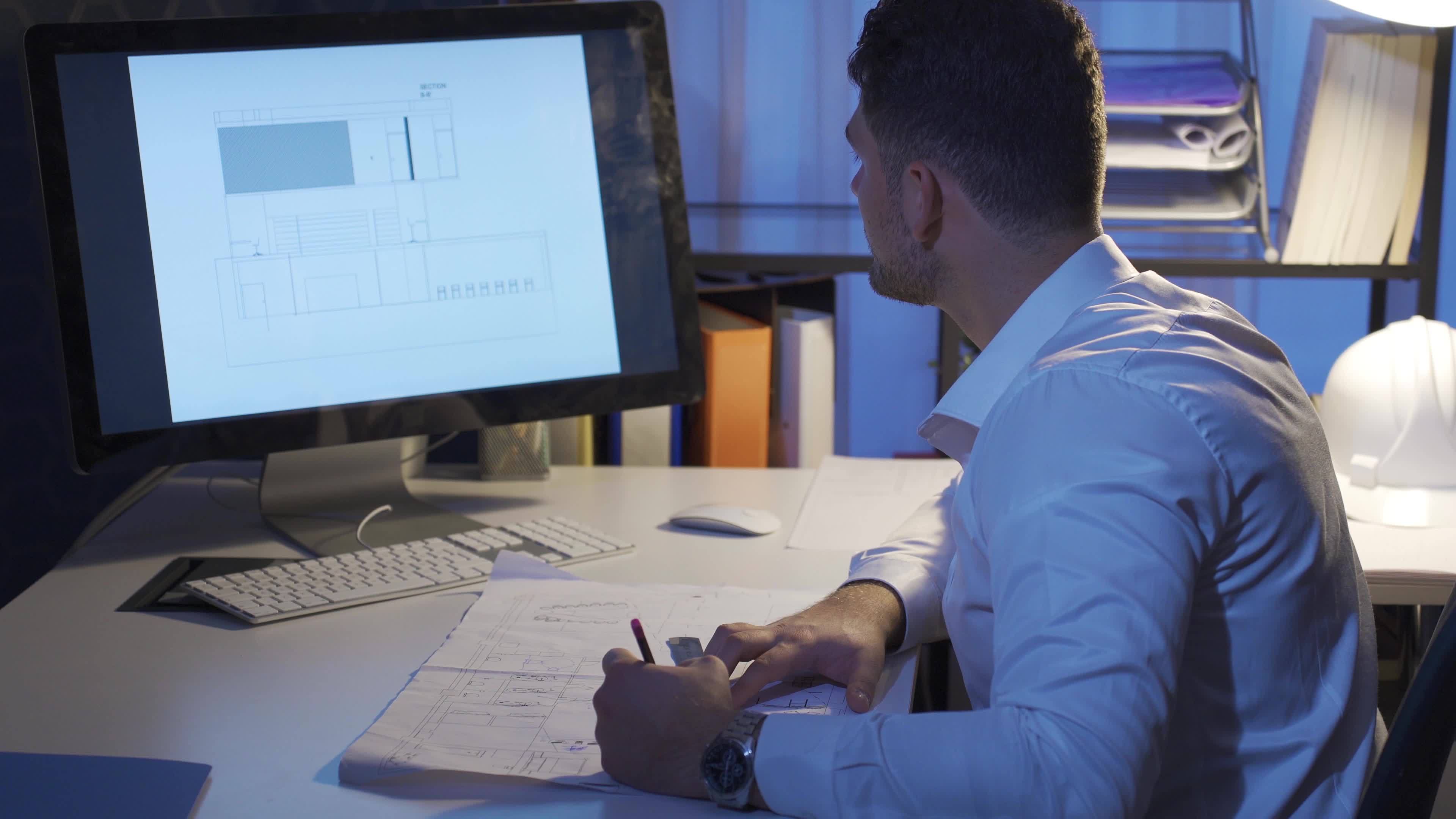 Young Male Designer Sitting At Desk And Drawing On A House Plan Young Male Designer Sitting At Desk And Drawing On A House Plan