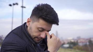 stressato uomo nel città riflessivo e preoccupato. città fatica. il uomo è seduta su il panchina all'aperto nel il città e è preoccupato e depresso perché di il suo pensieri. video