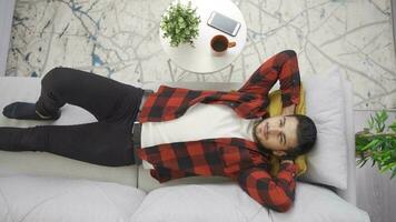 Young man lying alone on the sofa in his modern home and daydreaming about the future. Man lying on sofa at home resting and comfortably dreaming, thinking and smiling. video