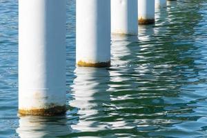 Rusty pier posts in salt sea water. White columns diagonal. Pillars mount for bridge. Sunny weather. photo