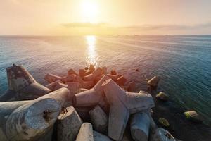 Beautiful sunset seascape. Breakwaters tetrapods ashore of pier. Cargo ships on the horizon. Travel dreams and motivation photo