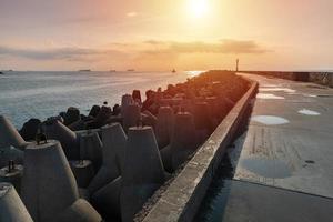 North pier with breakwaters, sunset seascape. Tetrapods along edges of pier. Beautiful evening seascape. Modern lighthouse in sunlight. photo