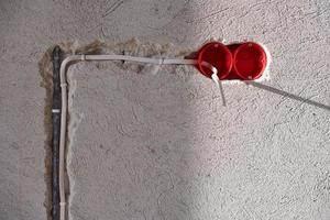 Plastic socket box and electrical wires on plastered wall photo