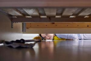 Woman cleaning floor under bed using flat wet mop. photo