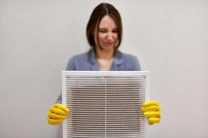 Woman holding dirty and dusty ventilation grille, disgusted photo