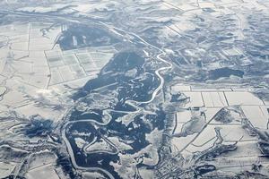 Aerial view over clouds top to snow covered rivers, fields and roads, winter fresh frosty air photo