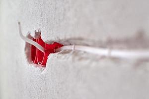 Plastic socket box and electrical wires on plastered wall photo