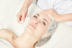 Beautician making facial massage with Gua Sha stone of woman face skin for lymphatic drainage photo