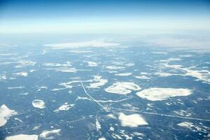 Aerial view from airplane window over clouds top to snow covered rivers, fields and roads photo