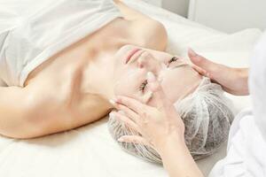 esteticista suaviza la máscara de hoja en la cara de la mujer para rehidratar la piel de la cara, procedimiento en el salón de belleza foto