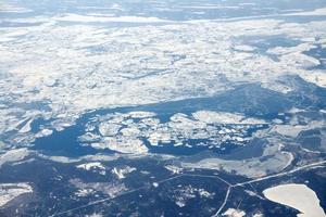 vista aérea desde la ventana del avión sobre las nubes hasta el mar helado cubierto de nieve, aire fresco helado de invierno foto