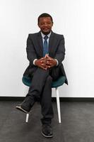 Smiling african american black man in business suit sitting on chair with crossed fingers photo