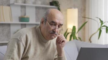 pensativo velho homem às computador portátil lidando com financeiro dificuldades enquanto pagando contas. pensativo velho homem sentado dentro frente do computador portátil lidando com financeiro dificuldades enquanto pagando contas. video