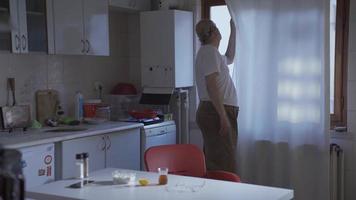 el antiguo hombre es mirando fuera el ventana a hogar. aburrimiento y soledad. el antiguo hombre quien abre el cortina y mira fuera el ventana mira fuera y quiere a claro su cabeza. video