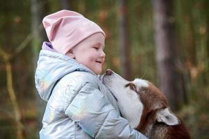 Cute little girl in pink hat and light blue jacket hugs Siberian Husky dog and smiling photo