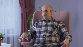 preocupado antiguo hombre obtiene estresado. antiguo hombre sentado en sofá solo a hogar y consiguiendo estresado por preocuparse. video