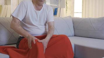 enfermo antiguo hombre tiene hueso y articulación esfuerzos. antiguo hombre con dolorido piernas, reumatismo. el antiguo hombre sentado en el sofá a hogar tiene articulación esfuerzos debido a su edad. video