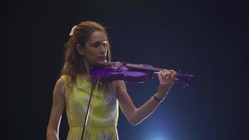 ung kvinna mästerligt spelar de fiol på en mörk skede. begåvad ung musiker kvinna spelar de fiol. opera eller musik hall. video