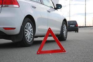 Road accident or vehicle breakdown - two cars white and black stopped on highway after collision. Red warning triangle in front of them, low angle shot photo