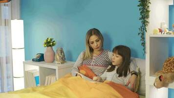 Mother and daughter reading a book in bed. Little girl is reading a book in her bed with her mother. Sleeping at night, reading fairy tales.
