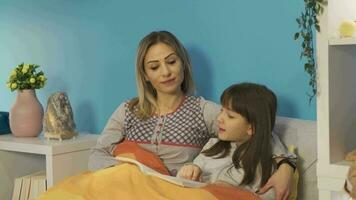 pequeño niña es leyendo un libro con su madre antes de yendo a dormir. pequeño niña es leyendo un libro en su cama con su madre. dormido a noche, leyendo hada cuentos. video