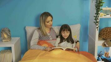 The girl is reading a book in the nursery. Mother daughter love. Little Girl is reading a book with her mother before going to sleep.