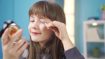 hermosa pequeño niña aprende a hacer arriba sí misma en el espejo. gracioso pequeño niña teniendo divertido aprendizaje a hacer maquillaje en frente de pequeño espejo en su habitación. video