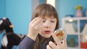 Funny cheerful little girl does her own makeup. The little girl who does her own make-up with the make-up materials she secretly bought from her mother is funny and entertaining. video