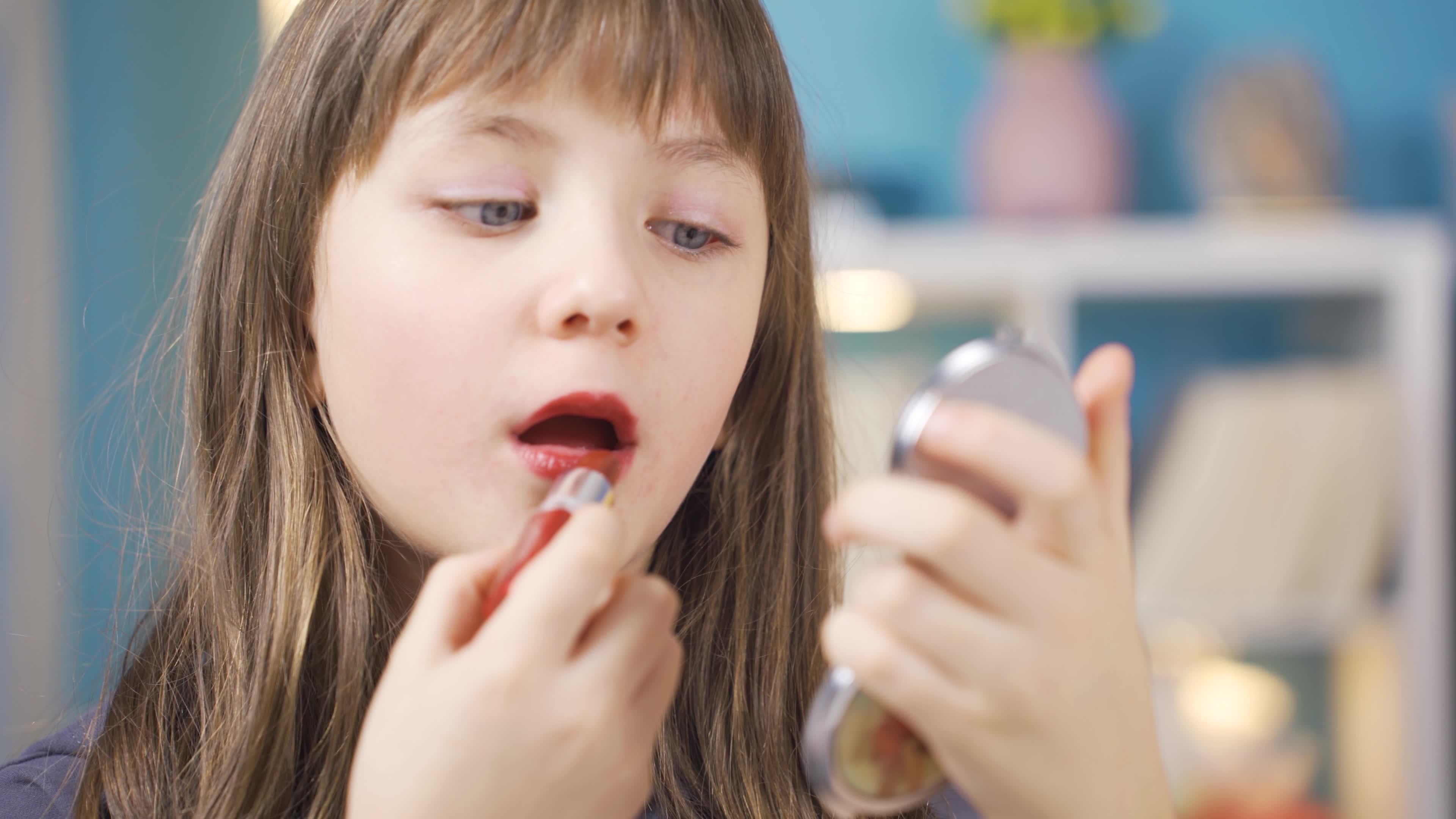 Cute funny little girl doing makeup. Putting lipstick on the lips. The