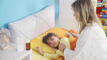 el devoto madre toma el fiebre de el enfermo pequeño muchacha. de la madre afecto. linda hermosa pequeño niña es enfermo y acostado en su cama, su madre es tomando su temperatura. video