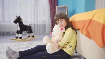 Unhappy and thoughtful little girl hugging her teddy bear in her room. Little girl hugging her teddy bear is unhappy and thoughtful. video