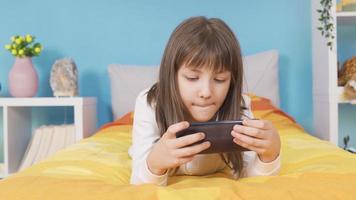 The little girl is playing with the phone. Phone addiction. The cute little girl who spends a lot of time on the phone every day is playing games. video