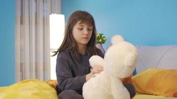 Unhappy and sad little girl alone in the room and hugging her teddy bear. The little girl who is left alone in her room is sad and hugs her teddy bear and is not feeling well. video