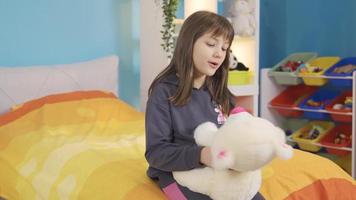 de weinig meisje, wie is alleen in haar kamer, praat naar haar teddy beer en maakt vrienden. schattig mooi weinig meisje pratend met haar teddy beer, verveeld en ongelukkig. video