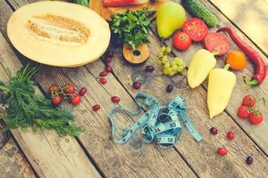 Fruits, vegetables and in measure tape in diet on wooden background. Top view. Toned image. photo