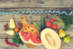 Fruits, vegetables and in measure tape in diet on wooden background. Top view. Toned image. photo