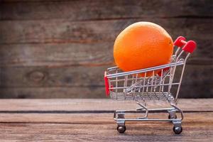 Shopping cart with orange on the old wood background. Toned image. photo