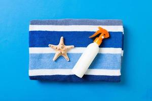Summer beach flat lay accessories. Sunscreen bottle cream, towel and seashells on colored Background. Travel holiday concept with copy space photo