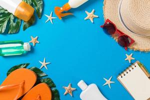 Beach accessories with straw hat, sunscreen bottle and seastar on blue background top view with copy space photo