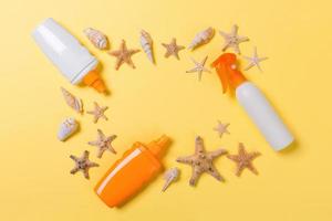 sunscreen cream with starfish and seashells in bottles on yellow background, top view photo